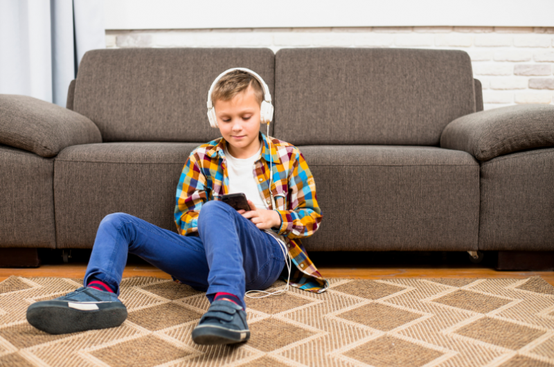 Fotobanka - Chlapec sedí na zemi, na ušiach má slúchadlá a hrá sa s mobilom